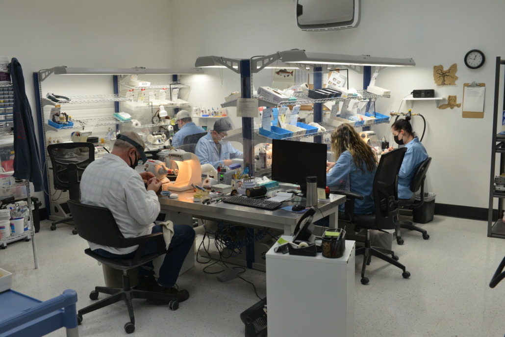 Picture of dental technicians working on dental restorations around a table in a dental lab.