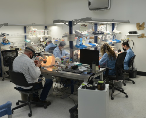 Picture of dental technicians working on dental restorations around a table in a dental lab.