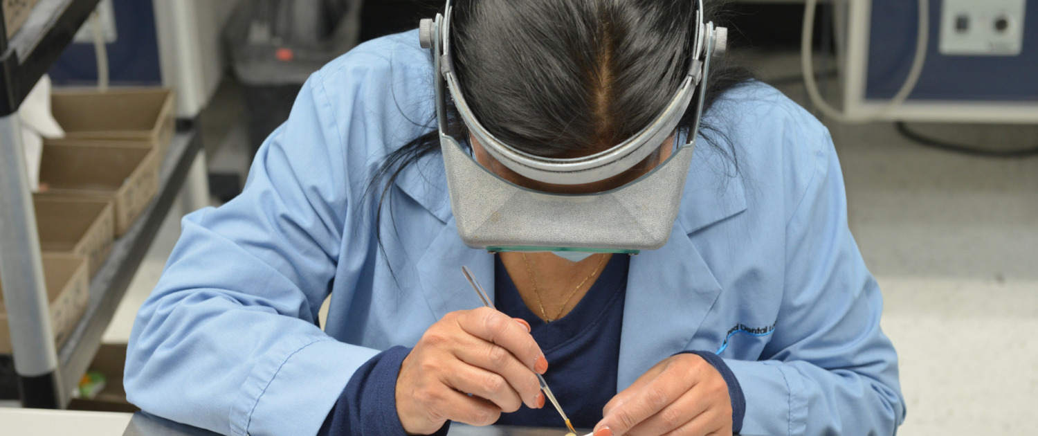Dental technician working on a dental implant from inside a laboratory.