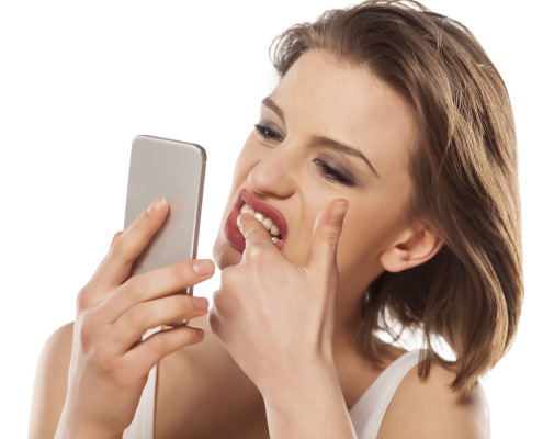 girl cleaning stains from her teeth using her smartphone as a mirror