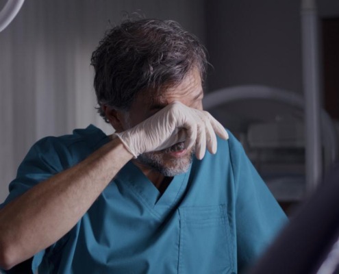 A still photo of a dentist rubbing his eyes tirelessly.