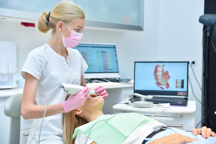 Orthodontist scanning patient's teeth with dental intraoral scanner and controls process on laptop screen.