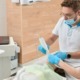 A man holds a piece of dental equipment and is examining a patient's teeth, with a dental assistant watching closely.